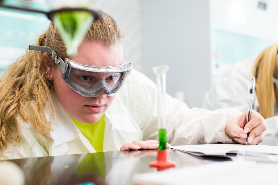 Young woman examines beaker content while taking notes.