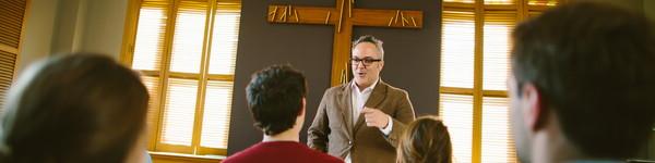 University Minister in chapel with students seated listening.